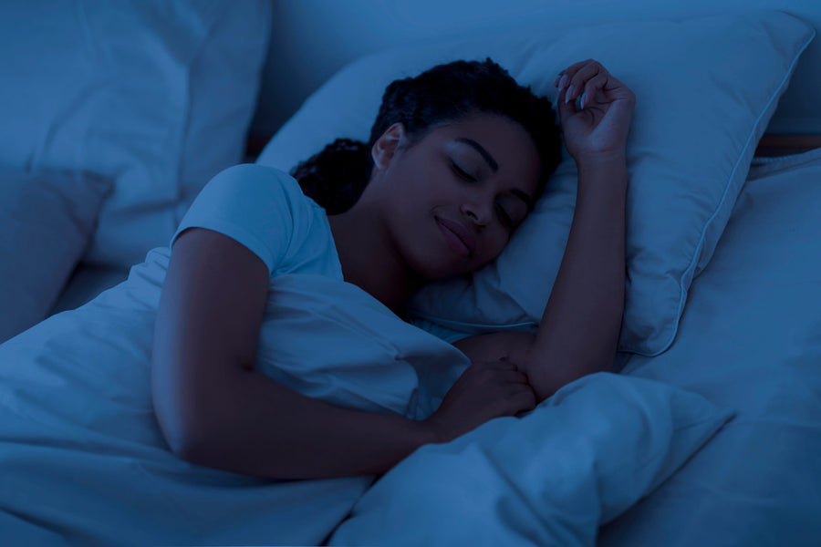 Woman sleeping comfortably on her side in a dark room, resting her head and arm on a white pillow.
