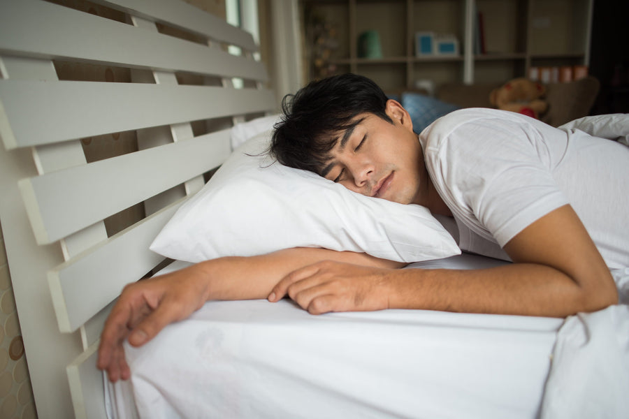 Man sleeping peacefully on his side, his head properly supported by a comfortable white pillow in a bright bedroom.