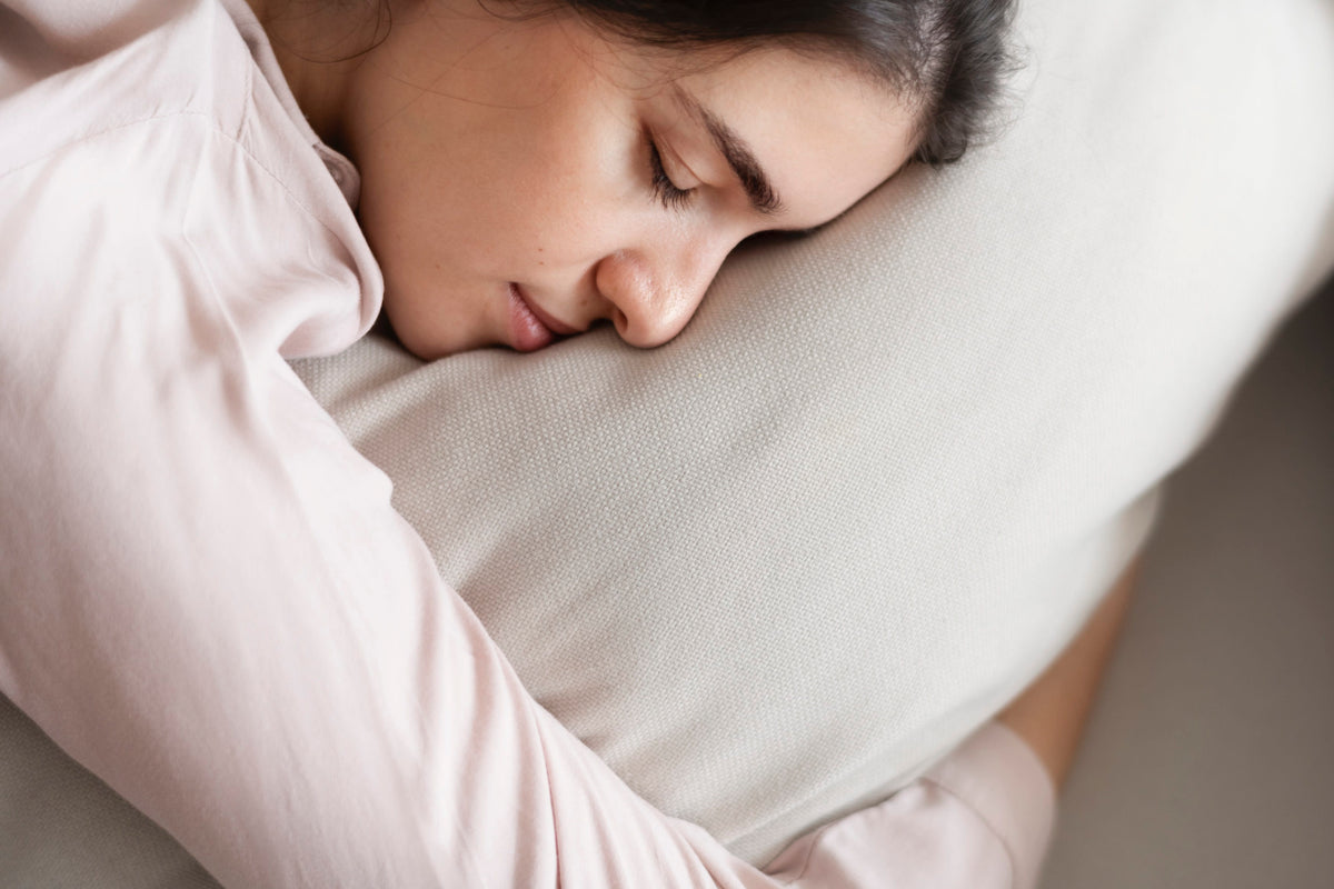 A woman sleeps soundly on her side, resting her face on a large, white pillow.