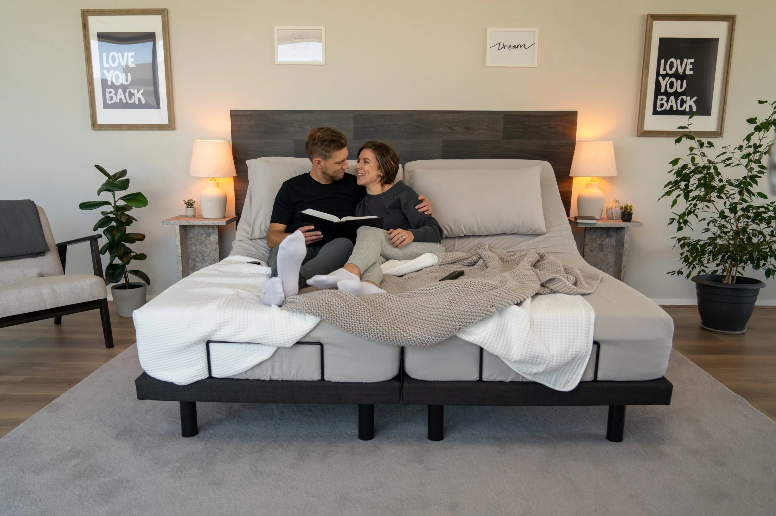 A couple reads a book together while sitting up comfortably on a split adjustable bed, with the head of each side elevated.