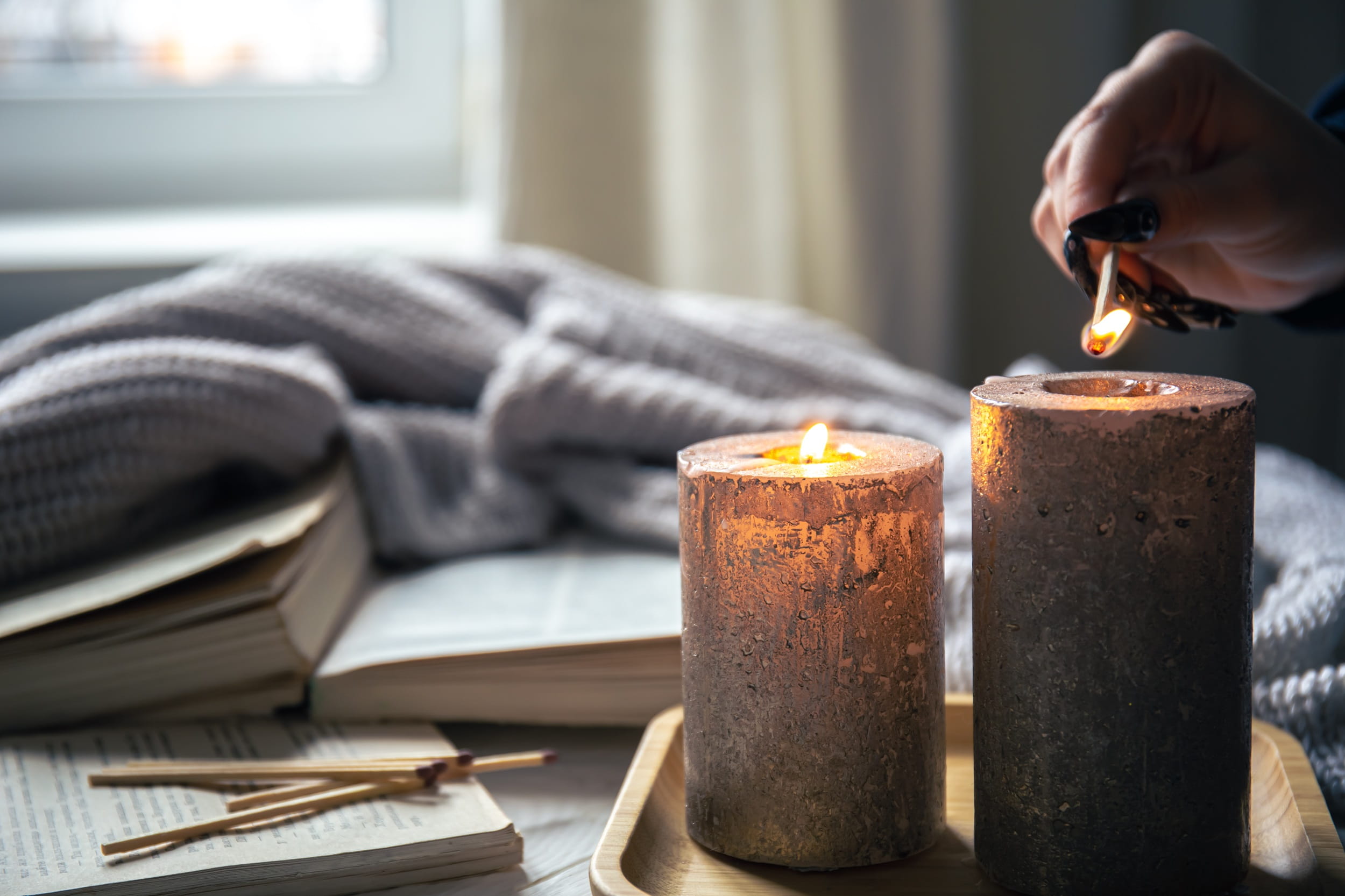 Hand lighting a candle next to an open book, depicting cozy reading and self-care new year resolutions ideas