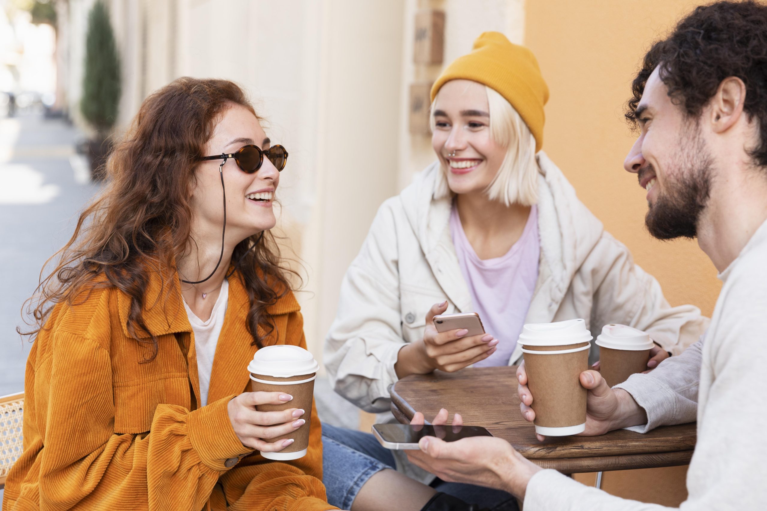 Friends laughing and drinking coffee at an outdoor cafe, illustrating social connection New Year's resolutions ideas