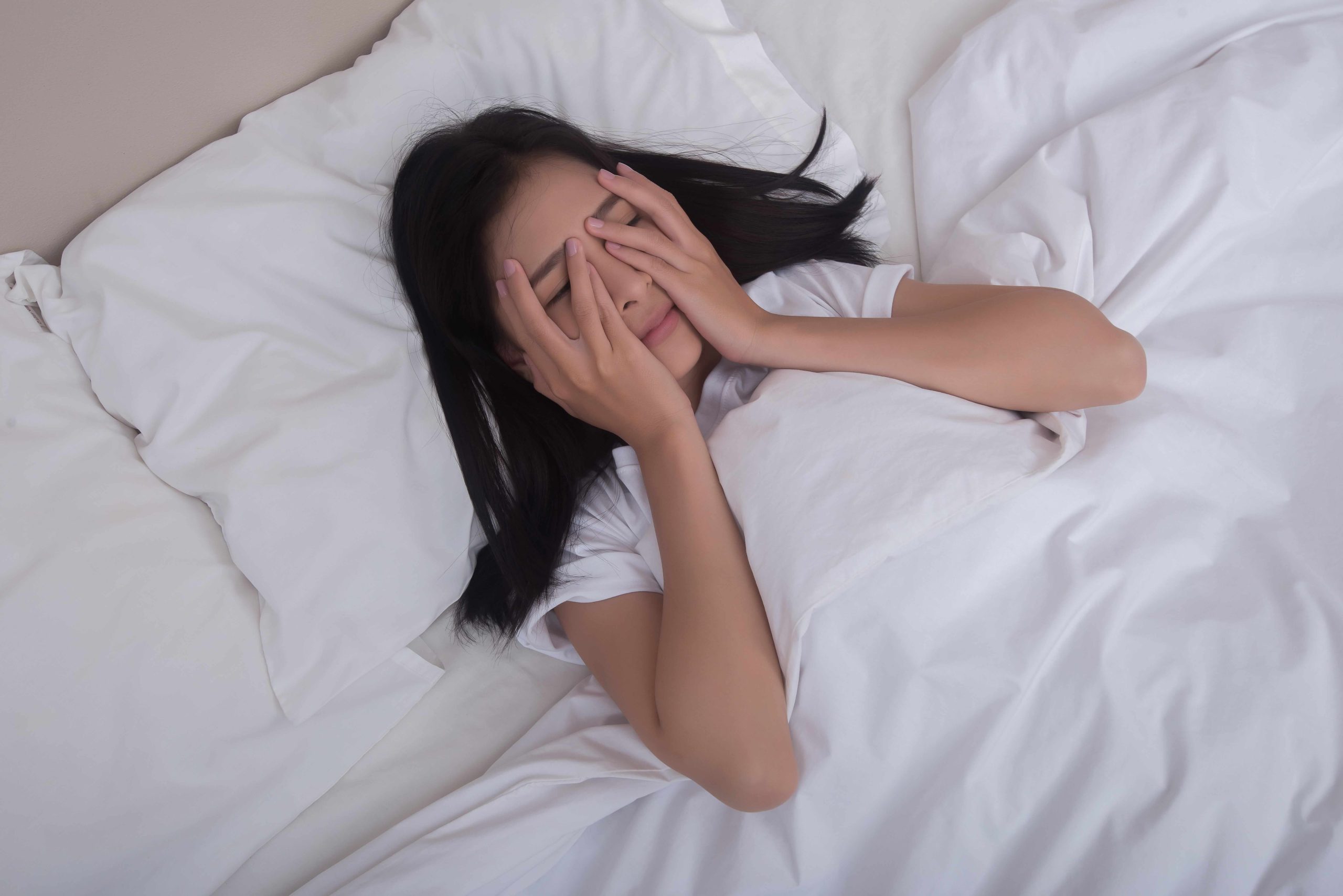A woman lying in bed with her hands covering her face, looking distressed and unable to sleep due to nighttime anxiety.