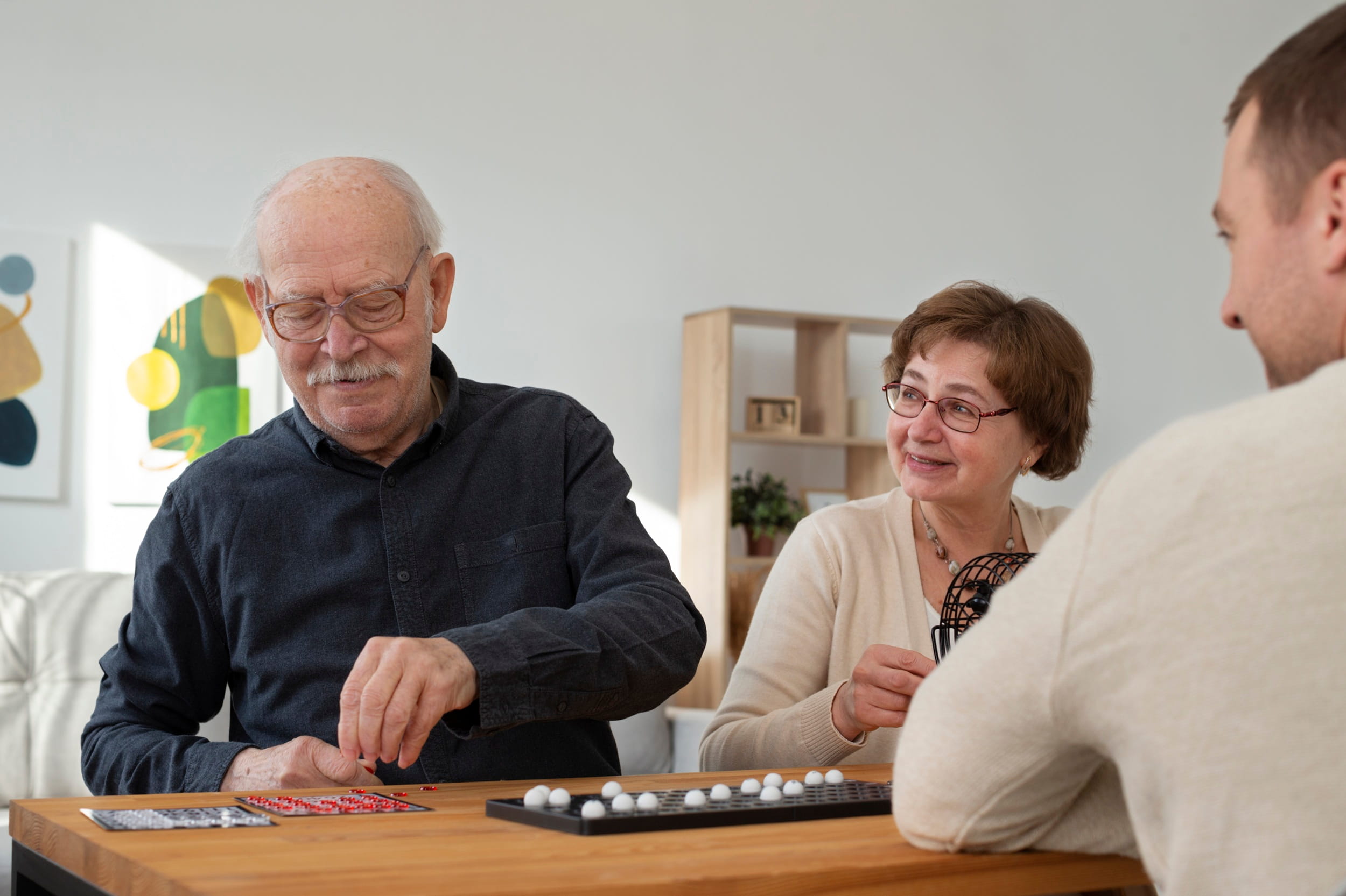 An older man and woman smiling while playing a board game with a younger man, illustrating healthy cognitive aging