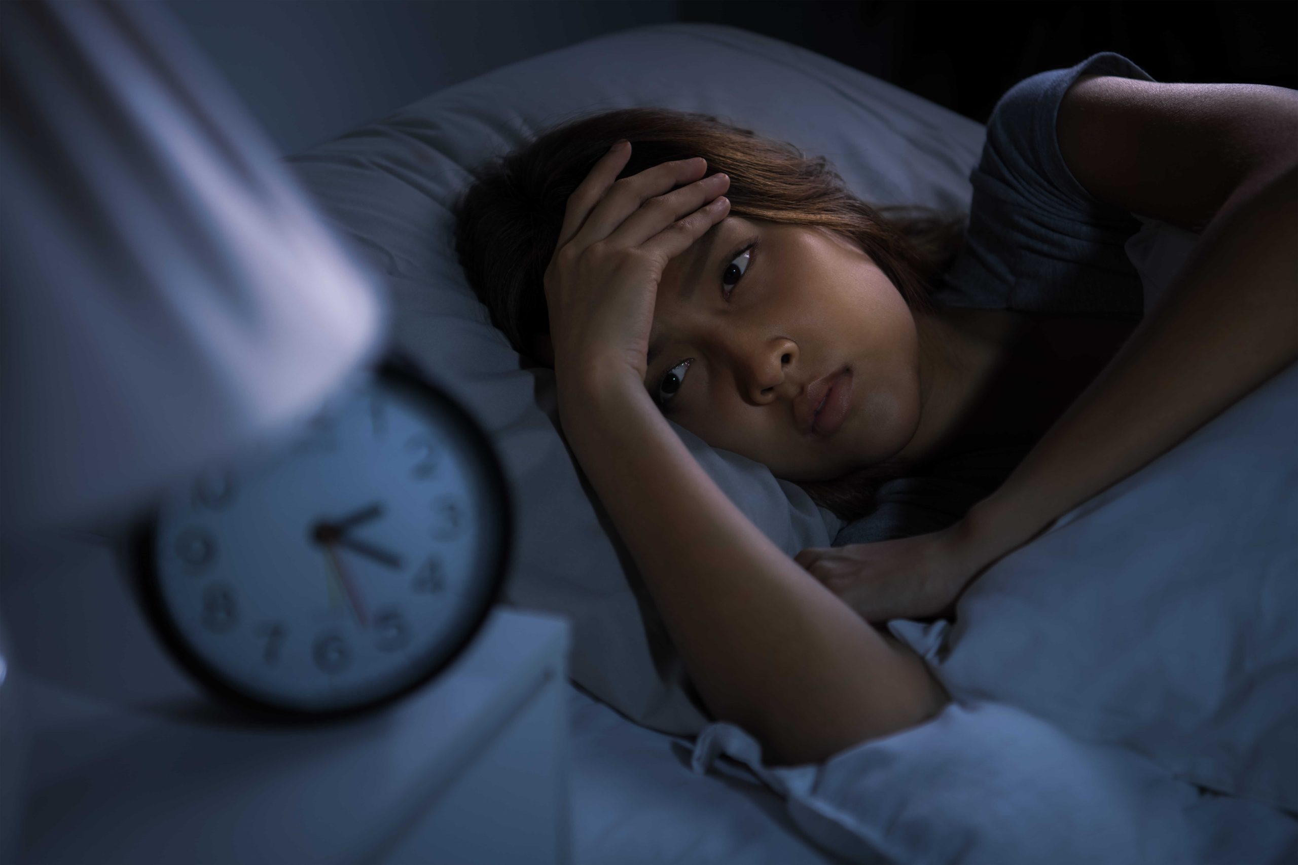 A person lying awake in the dark staring at a bedside clock, illustrating the frustration of broken sleep and racing thoughts.