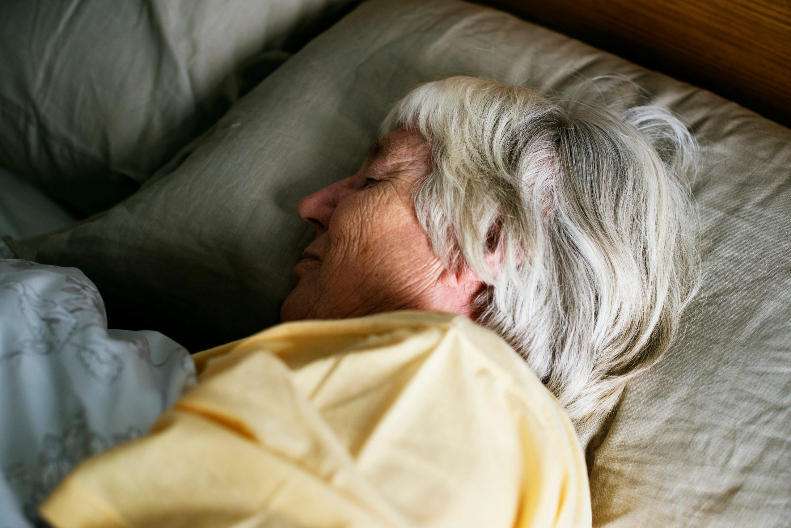 Close-up of an older woman sleeping peacefully in bed, representing the deep sleep needed for the brain's cleaning cycle