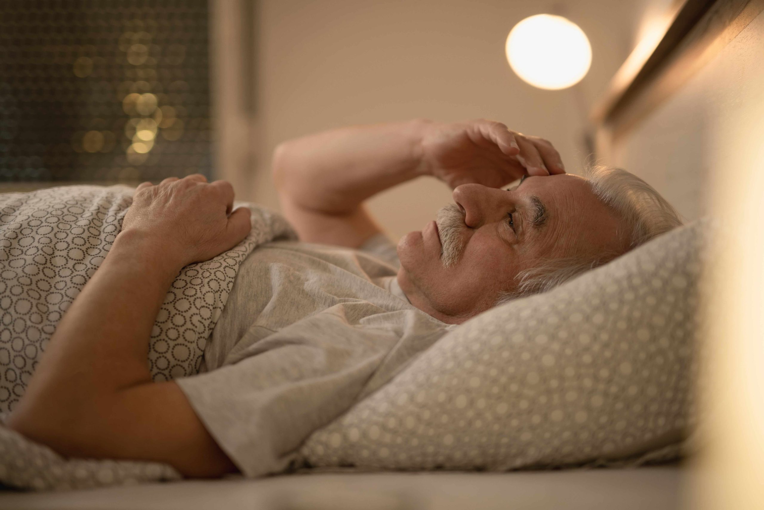 An older man lying in bed looking worried, representing the unique sleep-related anxiety and frequent night waking faced by older Australians.